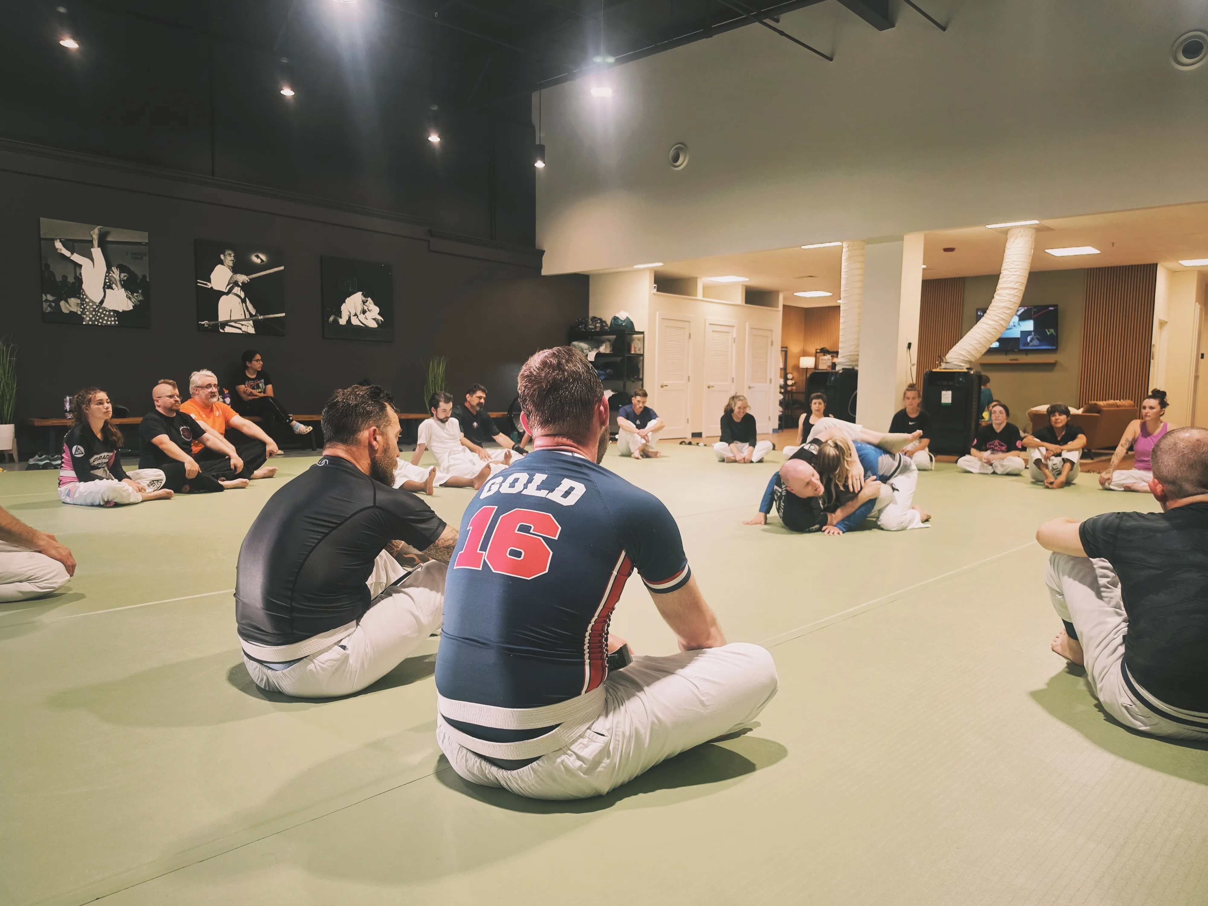 Students gathered in a circle watching a technique demonstration on the mat.