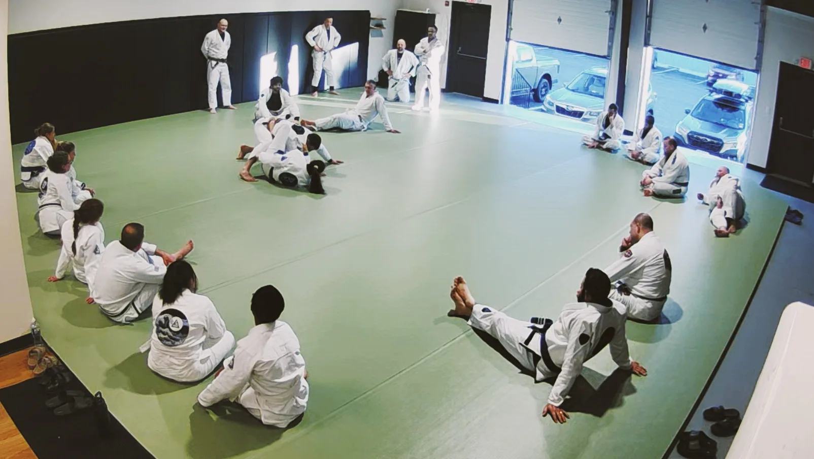 A Master Cycle class watching a technique demonstration in a circle on the mat.